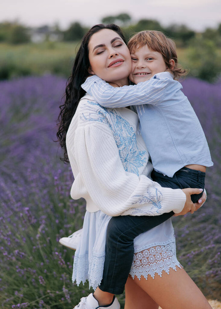 Счастливые мать и сын обнимаются на фоне цветущей лаванды. Крупный план. - Фото, изображение