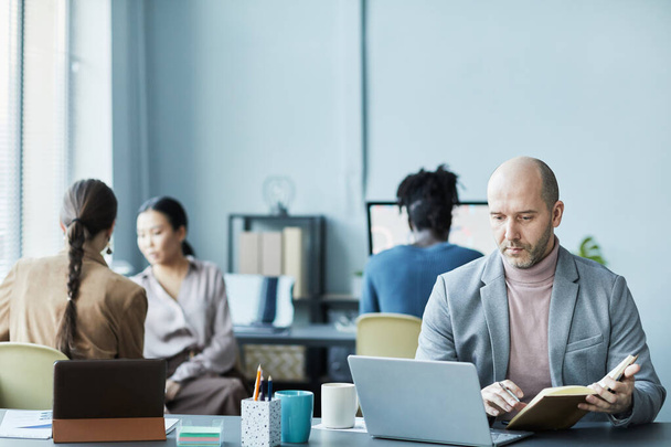 Портрет облисіння зрілого чоловіка, що працює з ноутбуком в офісі і дивиться на зосереджений екран, копіює простір - Фото, зображення