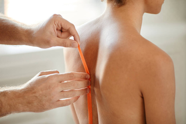 Primer plano del terapeuta de rehabilitación poner cinta adhesiva en la espalda de la mujer joven para aliviar el dolor muscular, espacio de copia - Foto, imagen