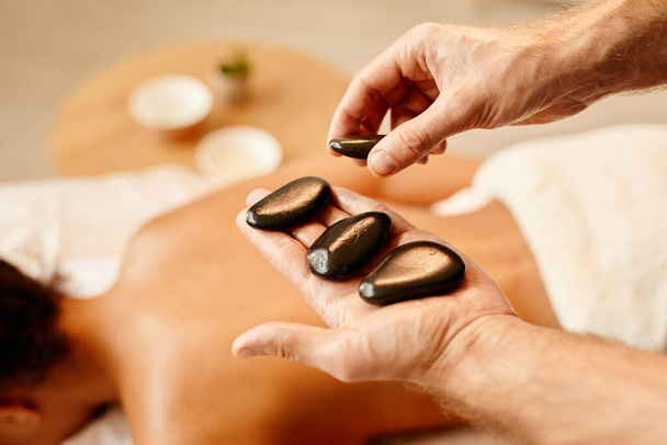 Close up of male hands laying stones on back of young woman in relaxing SPA session, copy space - Photo, Image