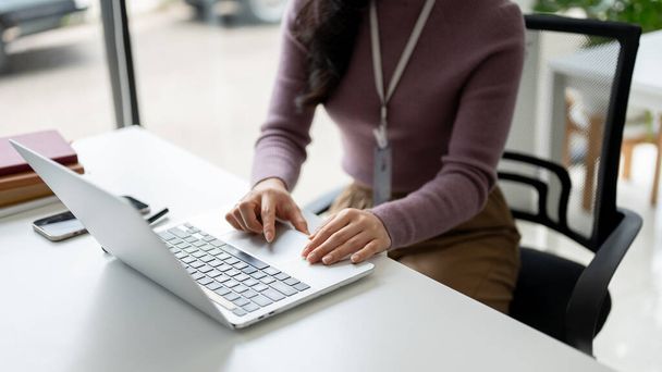Κοντινή εικόνα μιας εργαζόμενης επιχείρησης ή μιας εργαζόμενης γυναίκας που χρησιμοποιεί τον φορητό υπολογιστή της για να διαχειριστεί την επαγγελματική της εργασία στο γραφείο της στο γραφείο. - Φωτογραφία, εικόνα