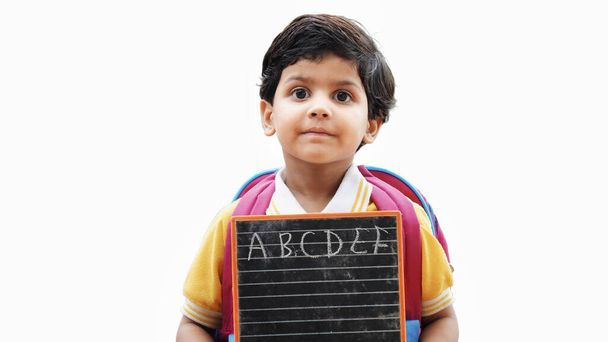 Ritratto di felice carina bambina indiana in uniforme scolastica con ardesia bianca sullo sfondo, adorabile bambino elementare che mostra lavagna nera. concetto di educazione dei bambini. india rurale. - Foto, immagini
