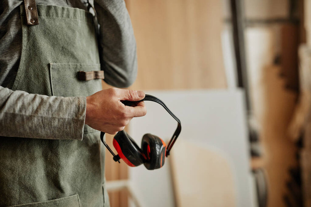 Primer plano del trabajador que sostiene auriculares de cancelación de ruido en taller, producción y seguridad, espacio para copias - Foto, Imagen