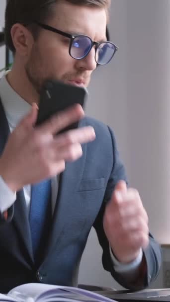 Un giovane banchiere impegnato investimento di aspetto americano sta parlando al telefono mentre si lavora su un computer. Gestore impegnato. Lavoro in ufficio - Filmati, video