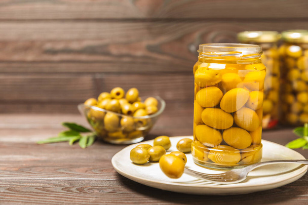 Delicious green olives. Pickled olives in glass jar. On a wooden background.Tasty olives. Close-up. Vegan.Place for text. copy space. - Foto, afbeelding