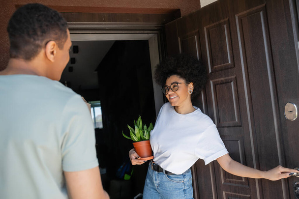 uśmiechnięta Afroamerykanka z rośliną otwierającą drzwi do nowego domu w pobliżu zamazanego chłopaka - Zdjęcie, obraz