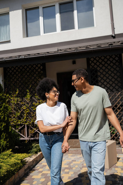 smiling african american woman holding hand of boyfriend in sunglasses near new house - Foto, afbeelding