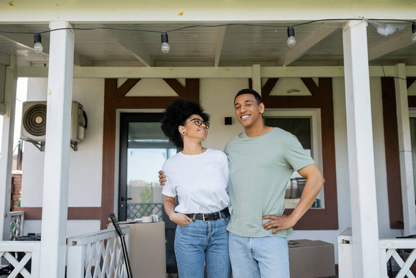 mosolygó afro-amerikai pár ölelés közben áll a verandán az új ház - Fotó, kép