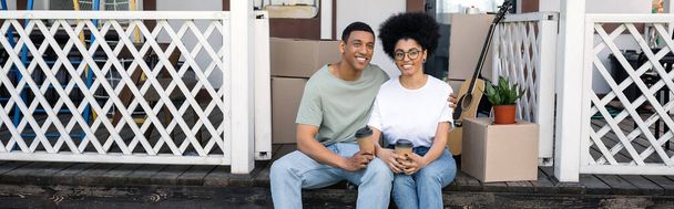 positive african american couple with takeaway coffee sitting together on porch of new home, banner - Photo, Image