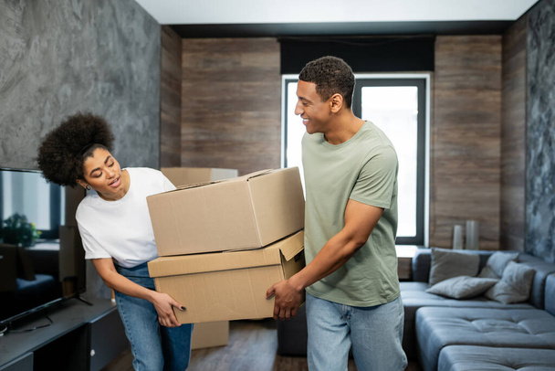 sorridente coppia afro-americana che tiene scatole di cartone durante lo spostamento in soggiorno - Foto, immagini