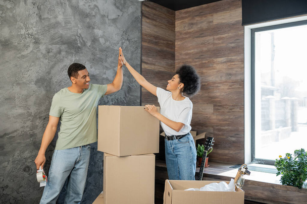 allegra coppia afro-americana dando alto cinque scatole di cartone vicino a nuova casa - Foto, immagini