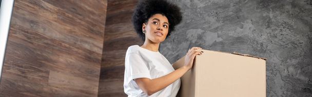 Αφροαμερικανή γυναίκα κοιτάζει μακριά κοντά σε χαρτοκιβώτιο κατά τη διάρκεια της μετακόμισης στο νέο σπίτι, banner - Φωτογραφία, εικόνα