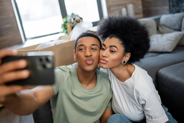 african american couple pouting lips while taking selfie on smartphone in new house - Photo, Image