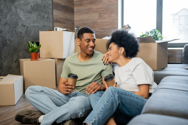 african american woman smiling at boyfriend with coffee near carton packages in new house - 写真・画像