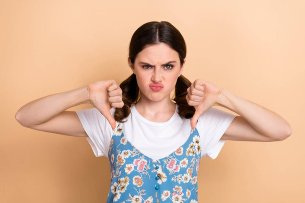 Portrait of funny dissatisfied woman ponytails hairdo dressed white shirt showing thumbs down dislike isolated on beige color background. - Fotografie, Obrázek