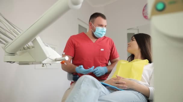 El dentista habla sobre la instalación de implantes. Una paciente femenina en la clínica de odontología. Concepto de tratamiento dental - Imágenes, Vídeo