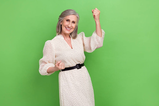 Photo of shiny lucky woman dressed beige outfit rising fists achieving success isolated green color background. - Фото, изображение