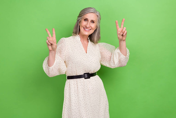 Photo portrait of beautiful grandma v-sign two fingers hands gesture wear trendy white outfit isolated on green color background. - Fotó, kép