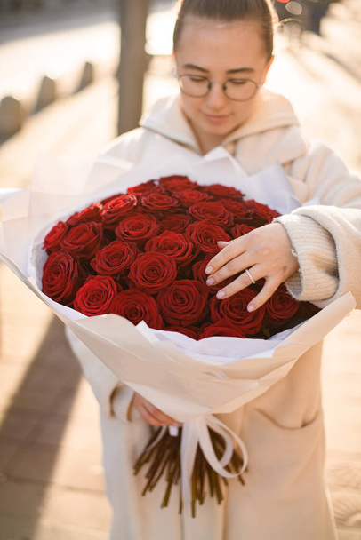 Young girl gently holding luxury bright bouquet of garden red roses in white craft wrapping paper. Present for loved one concept - Photo, Image