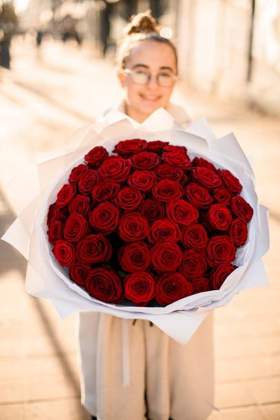 Big classy bright bouquet of red roses in hands of cute girl florist. Flowers in craft wrapping paper. Flowers shop concept - Fotografie, Obrázek