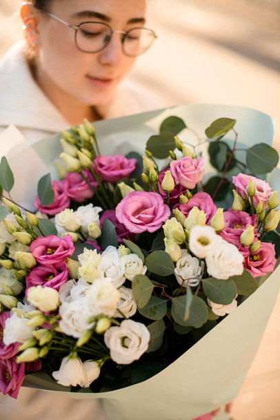 Mix of fresh eustoma flowers in cream and pink colors formed with craft wrapping paper in woman florists hands. Close up view. Blurred background - Foto, immagini