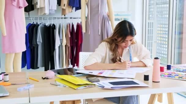 Beautiful Asian female fashion designers or dressmakers make the design of the new collection with samples of fabrics and sketches on paper. Fashion designer working in studio. Small business concept. - Footage, Video