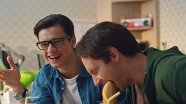 Lachen jongens reageren emotioneel tijdens lunchpauze close-up. Moderne ontwerpers die stokbrood eten en plezier hebben in hipster interieur. Twee makers genieten van maaltijd met een goed gesprek stemming op het werk plaats - Video