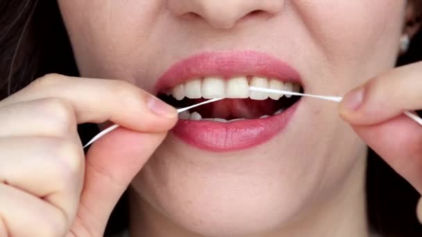 Žena si čistí zuby zubní páskou zblízka. Malá vzdálenost mezi zuby. - Záběry, video