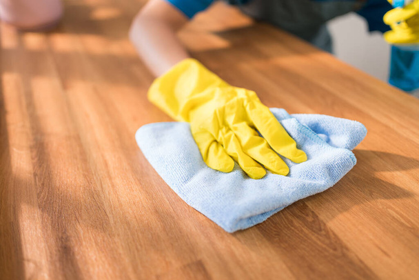 Zbliżenie profesjonalnych rąk Azjatki sprzątającej w żółtych gumowych rękawiczkach, używającej szmaty do wycierania drewnianej blatu kuchennego w domu. Sprzątanie, sprzątanie. - Zdjęcie, obraz