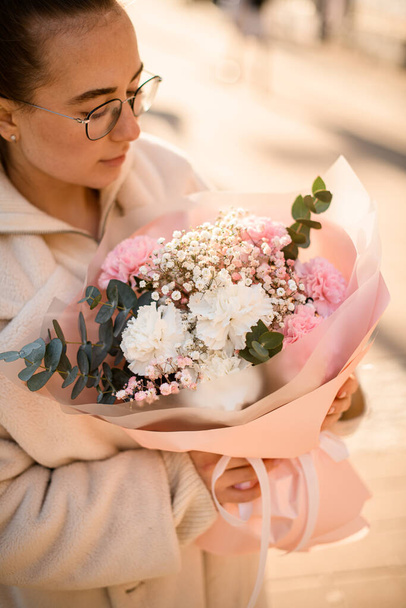 Young brunette woman holding huge beautiful bouquet of fresh pink and white carnations and green eucalyptus branches in wrapping paper. Flower shop concept. Vertical view - Foto, immagini