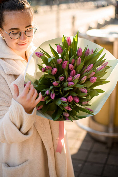 Fiatal gyönyörű nő kezében finom csokor rózsaszín friss tulipán a kezében. Egy csokor tavaszi virág női kézben. - Fotó, kép