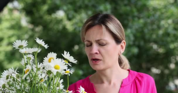 Γυναίκα με ανοιξιάτικο πυρετό φυσάει τη μύτη της σε χαρτοπετσέτα κοντά σε λουλούδια χαμομηλιού. Αλλεγία στα λουλούδια - Πλάνα, βίντεο