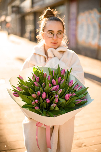Young brunette woman holding delicate bouquet of fresh pink tulips in hands. Bunch of fresh cut spring flowers in female hands - Фото, изображение