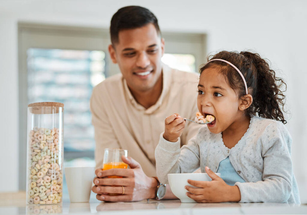 Eating, morning and a child with father for breakfast, food in the kitchen and care for nutrition. Smile, together and a young dad with a girl kid with cereal in a house for health and hungry. - Photo, Image