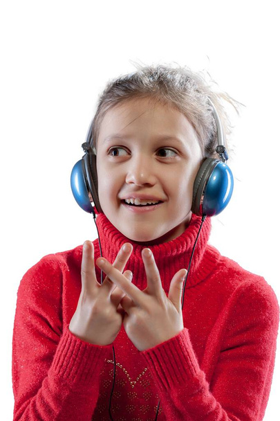 In einem roten Pullover hört ein munteres Mädchen über ihre blauen Kopfhörer Musik und tanzt und singt, während sie ihre künstlerischen Gefühle entwickelt. Lange braune Haare, weißer Hintergrund - Foto, Bild