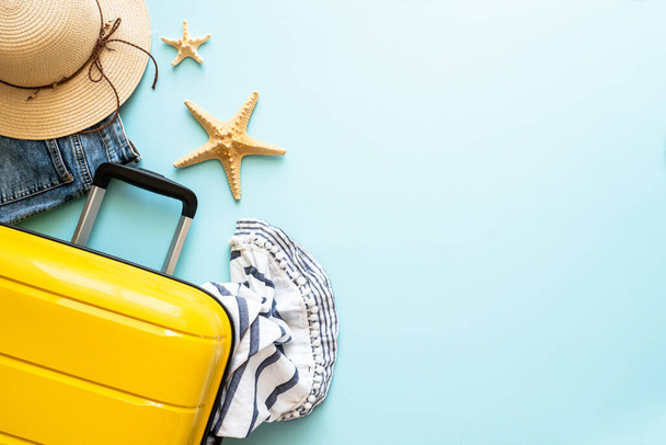 Ταξιδιωτικό υπόβαθρο, καλοκαιρινές διακοπές. Βαλίτσα, διαβατήρια, καπέλο και καλοκαιρινό ύφασμα σε μπλε φόντο. Επίπεδη εικόνα lay με αντίγραφο χώρου. - Φωτογραφία, εικόνα
