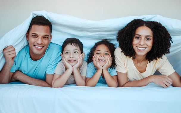Blanket, bed and portrait of parents with children for bonding, quality time and affection in morning. Love, family and happy mother, father and kids laying in bedroom for fun, playful and relaxing. - Photo, Image