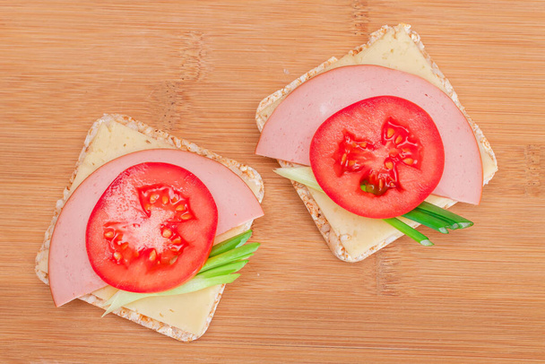 Rice Cake Sandwich with Tomato, Sausage, Green Onions and Cheese on Wooden Cutting Board. Easy Breakfast. Diet Food. Quick and Healthy Sandwiches. Crispbread with Tasty Filling. Healthy Dietary Snack - 写真・画像