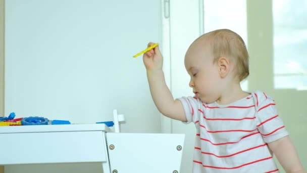 Bir yaşındaki bir çocuk tasarımcının parçalarını masadan yere atar. - Video, Çekim