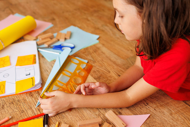 kind maakt een model van een vliegtuig van papier. De jongen is bezig met schaar en papier. het kind is thuis bezig met creativiteit. het kind droomt ervan piloot te worden. - Foto, afbeelding