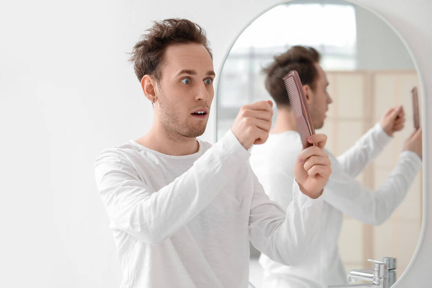 Shocked young man with comb and fallen down hair in bathroom - Fotó, kép