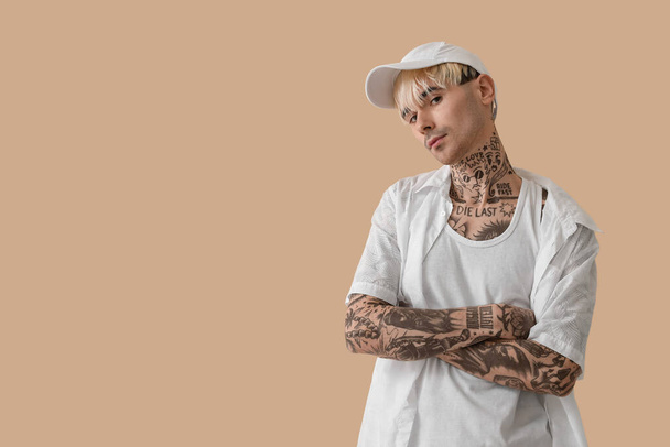 Hombre joven tatuado en gorra sobre fondo beige - Foto, Imagen