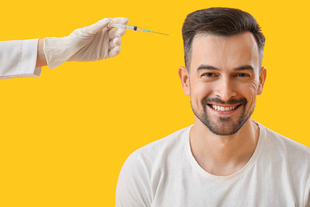Schöner Mann und Arzt mit Injektion für Haarwuchs auf gelbem Hintergrund - Foto, Bild