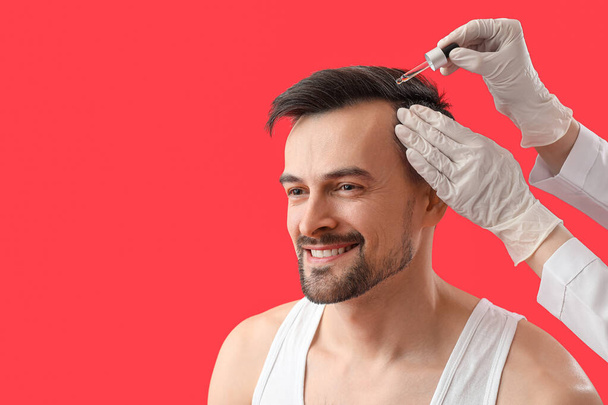 Beau homme recevant du sérum pour la croissance des cheveux sur fond rouge, gros plan - Photo, image