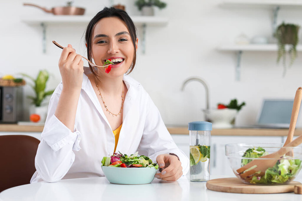 Jonge vrouw eet groentesalade in de keuken - Foto, afbeelding