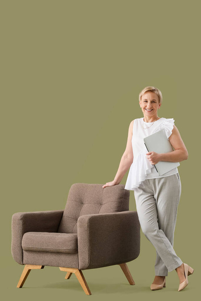 Mature psychologist with laptop and armchair on green background - Φωτογραφία, εικόνα