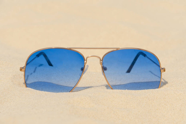 Las gafas de sol azules yacen en la arena. Vacaciones de verano, viajes y concepto de turismo. Descanso. Temporada de vacaciones - Foto, imagen