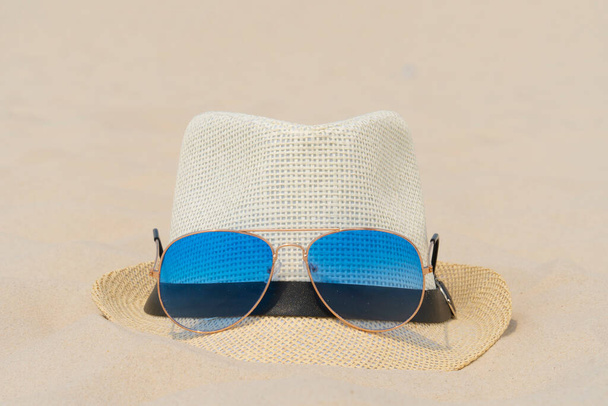 Blue sunglasses and a light hat lie on the sand. Summer vacation, travel and tourism concept. Summer rest. Holiday season - Фото, изображение