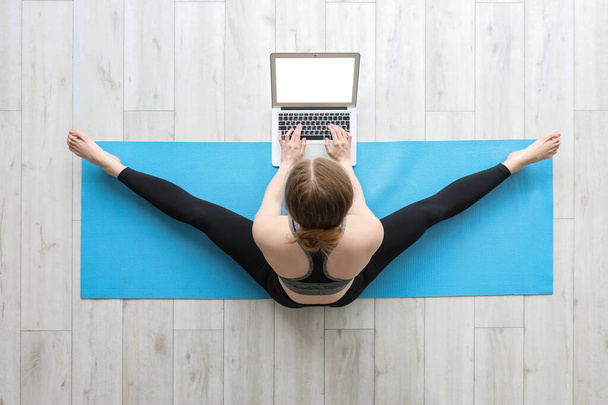 Giovane donna sportiva con laptop che fa yoga in palestra, vista dall'alto - Foto, immagini