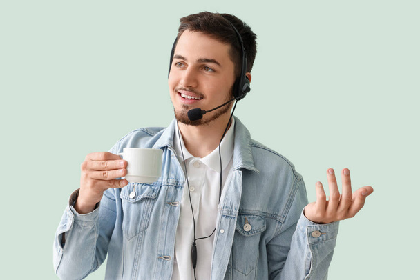 Male technical support agent with coffee on mint background - Foto, Imagen
